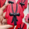 Red and black robe-shaped cookie held by a hand with more cookies in the background.