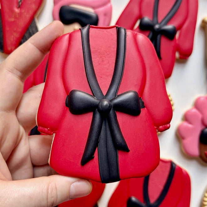 Red and black robe-shaped cookie held by a hand with more cookies in the background.